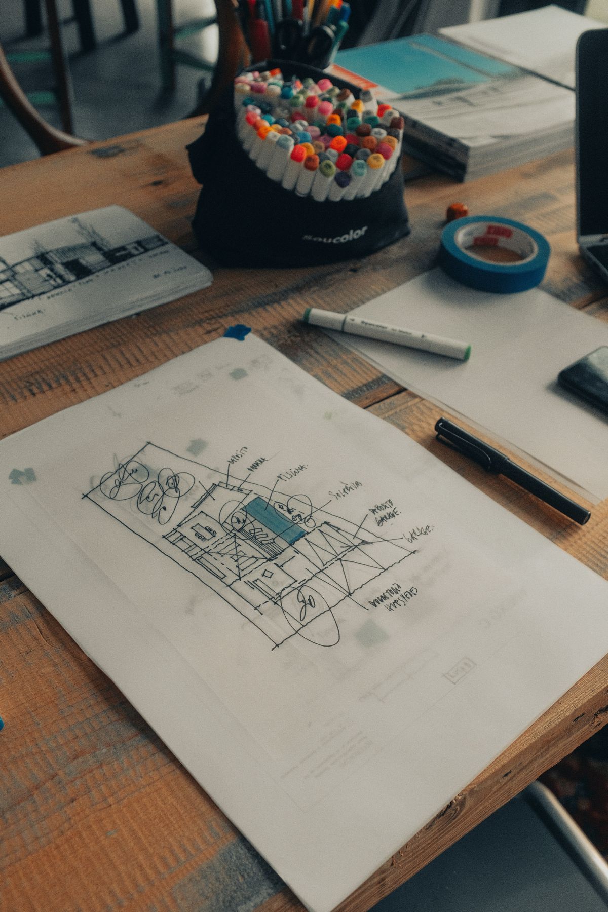 Pencil sketch of a storefront sign on a drafting desk with markers and pens